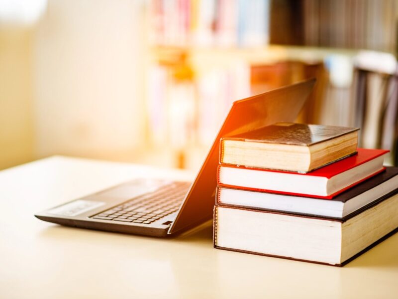 Bookshelves and laptops are placed on the library desk. Laptop and books in a scholarly, academic setting or school library